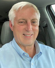 A white man with white hair wearing a blue shirt smiling.