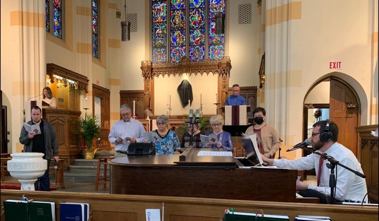 A church sanctuary with a piano and people singing standing behind the piano.