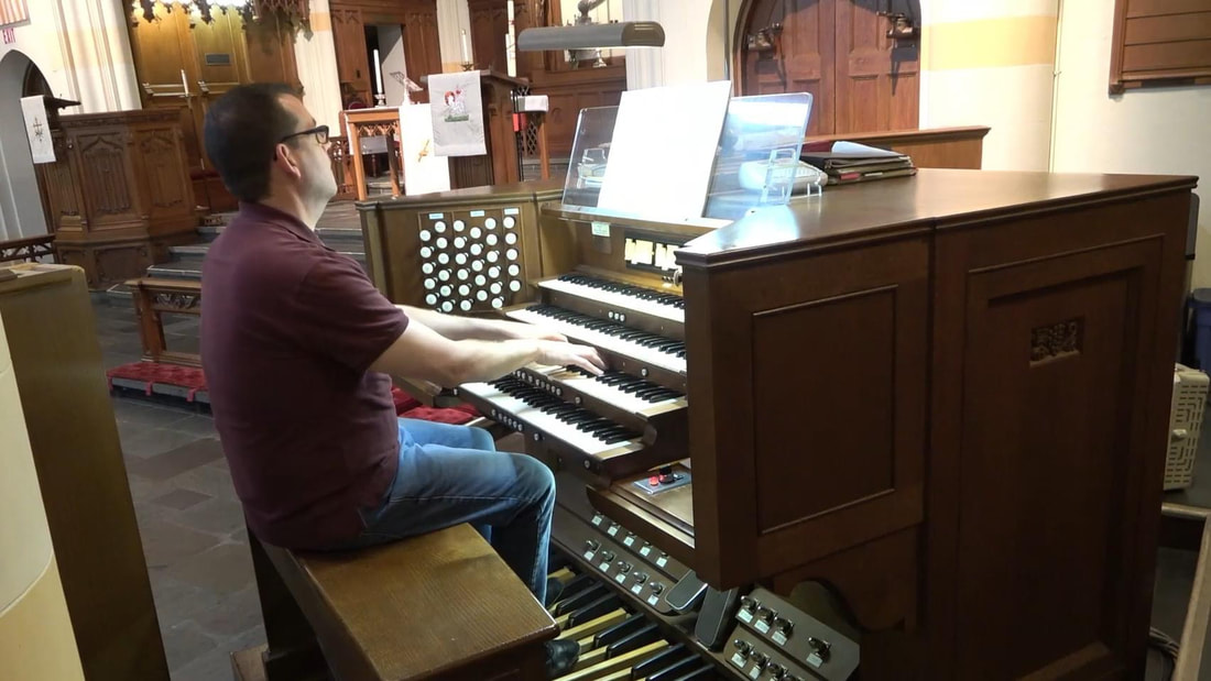 A man in a maroon shirt playing a pipe organ.