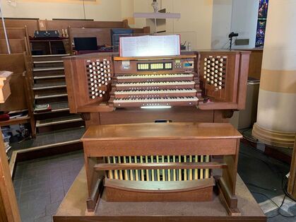 Pipe organ with three keyboard levels made of brown wood. It is located inside of a church